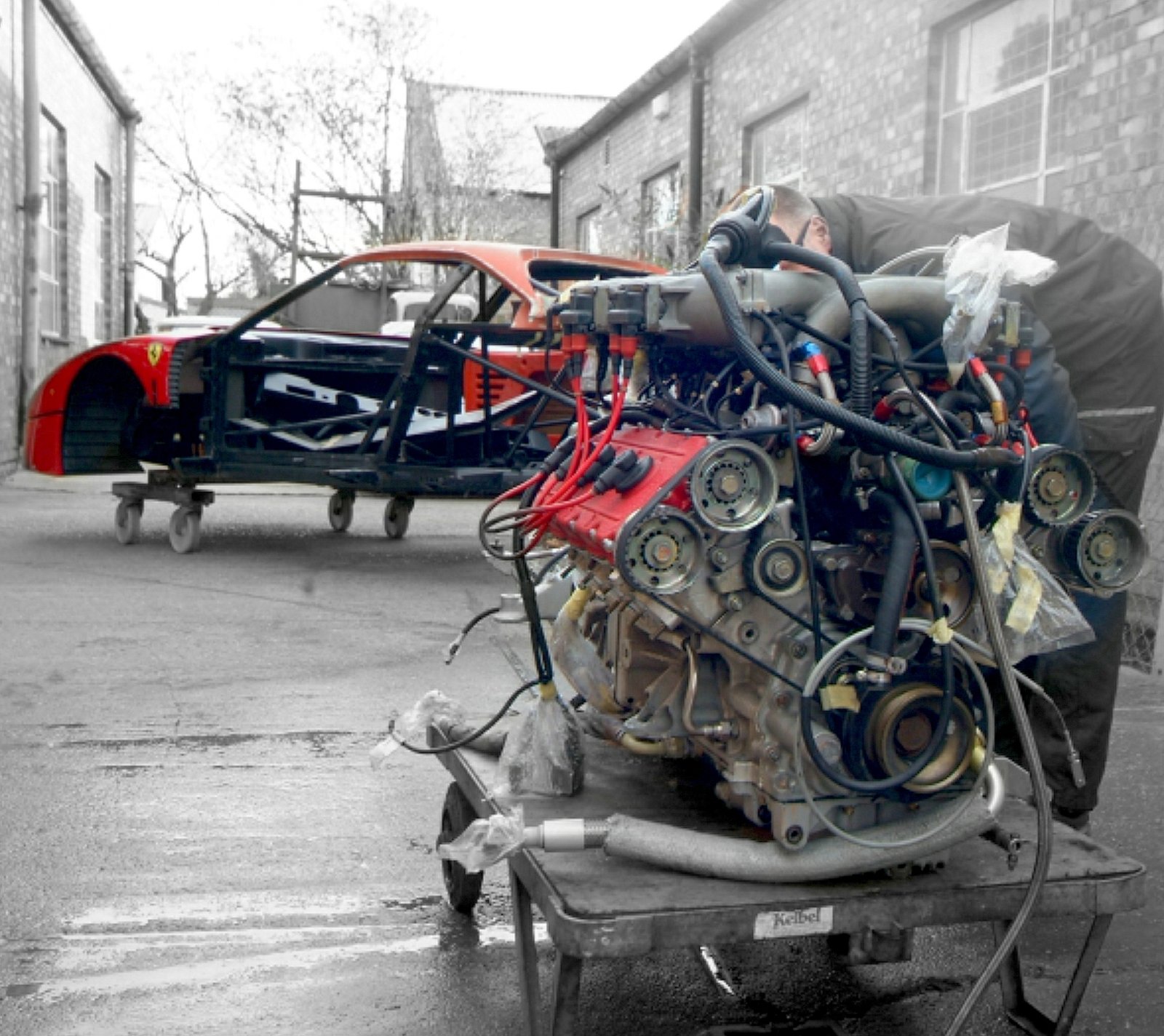 Removed Ferrari engine on a trolley beside a disassembled red car