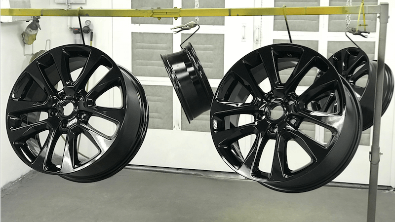 Black alloy wheels suspended from a rail in a finishing area