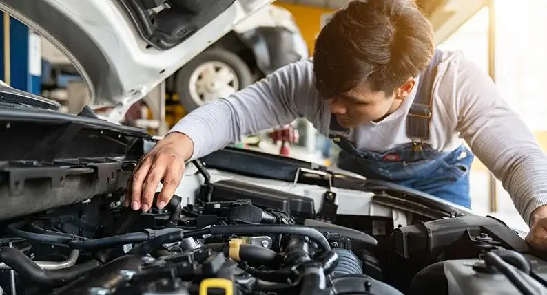 Technician inspecting components beneath a vehicle hood