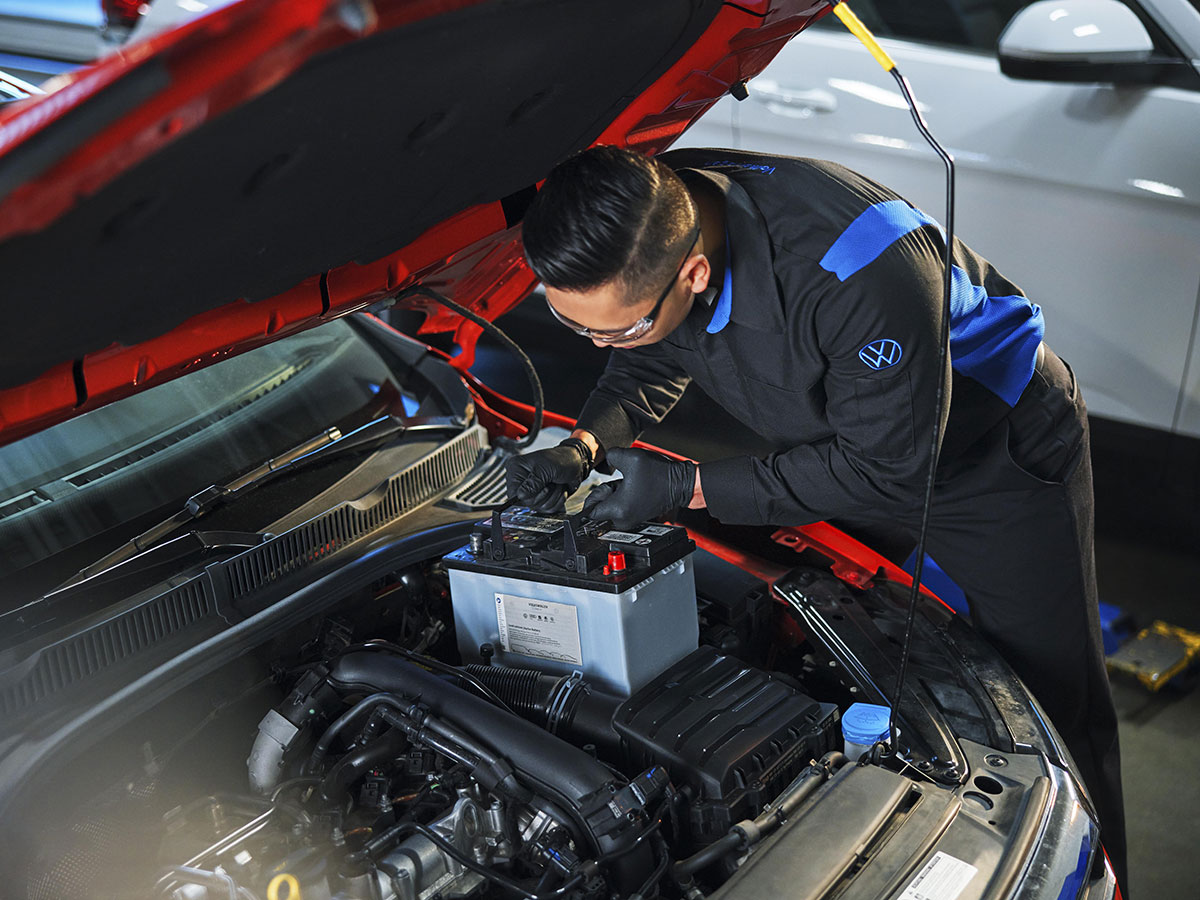 Technician testing the battery on a red Volkswagen in a workshop
