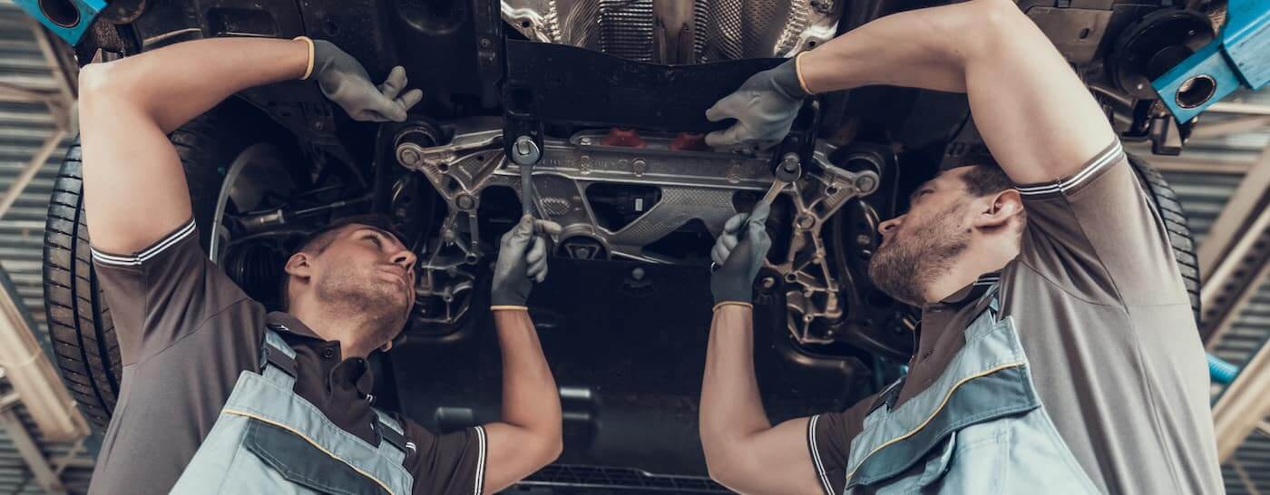 Technicians performing a physical Land Rover suspension inspection under a lift