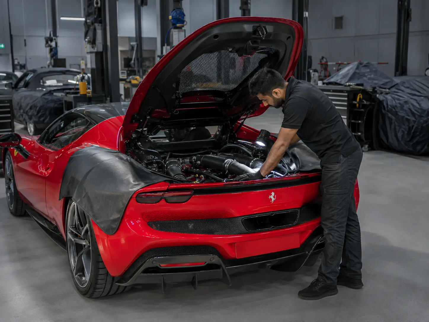 Technician inspecting the engine bay of a current Ferrari 296 in an independent workshop