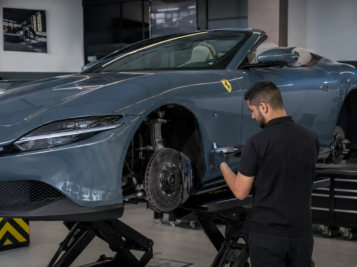 Technician inspecting brakes and suspension on a current Ferrari Roma in a workshop bay