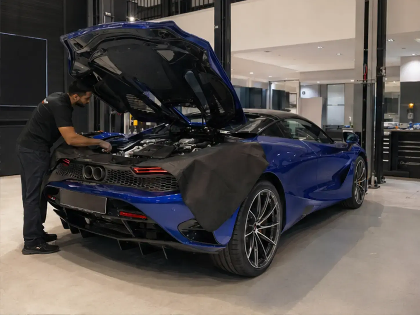 Technician visually inspecting engine-area and cooling components on a current McLaren 750S with protective covers