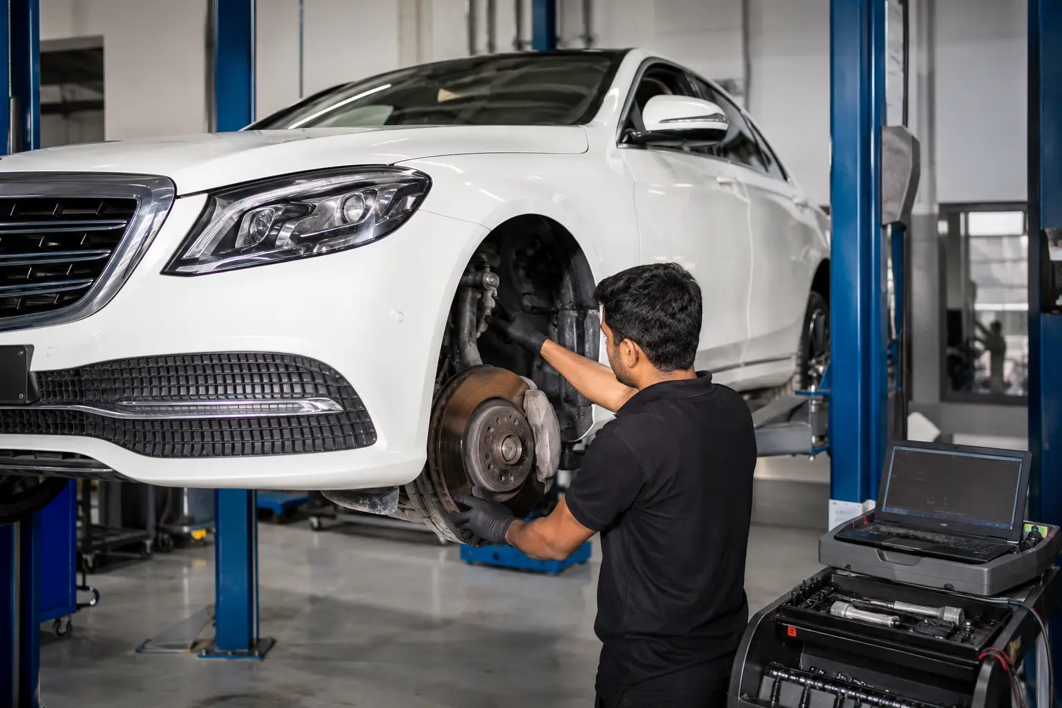 Technician inspecting steering and suspension components on a raised white Mercedes