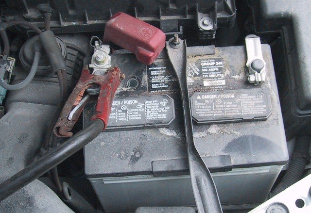 Battery positive terminal with a red clamp and a molded plus symbol on its raised cover
