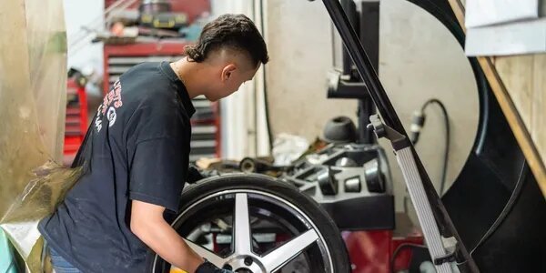 Technician handling a wheel and tire at a wheel balancing machine